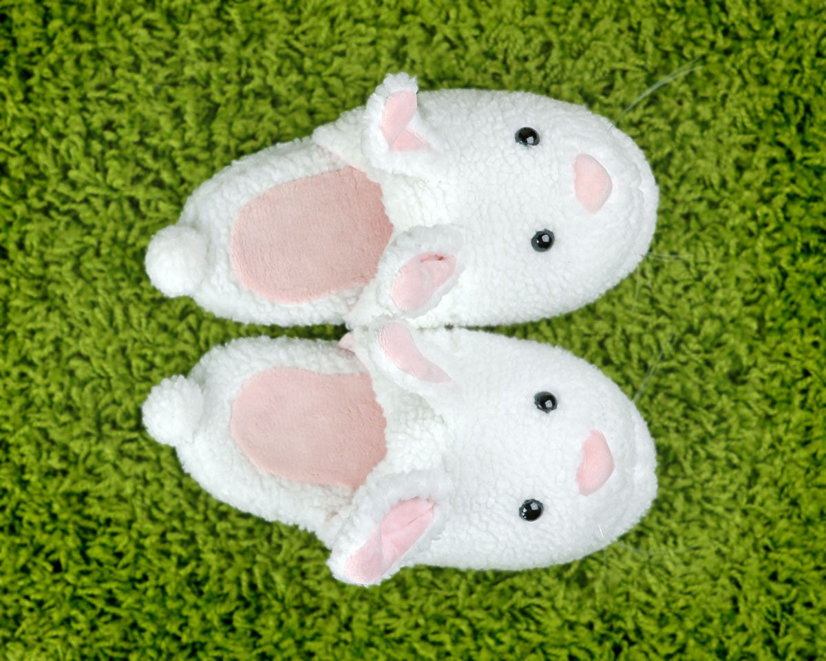 Pair of white plush slippers with pink accents on a green textured surface