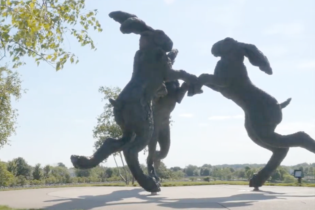 statue of three large hares dancing in a circle and holding paws