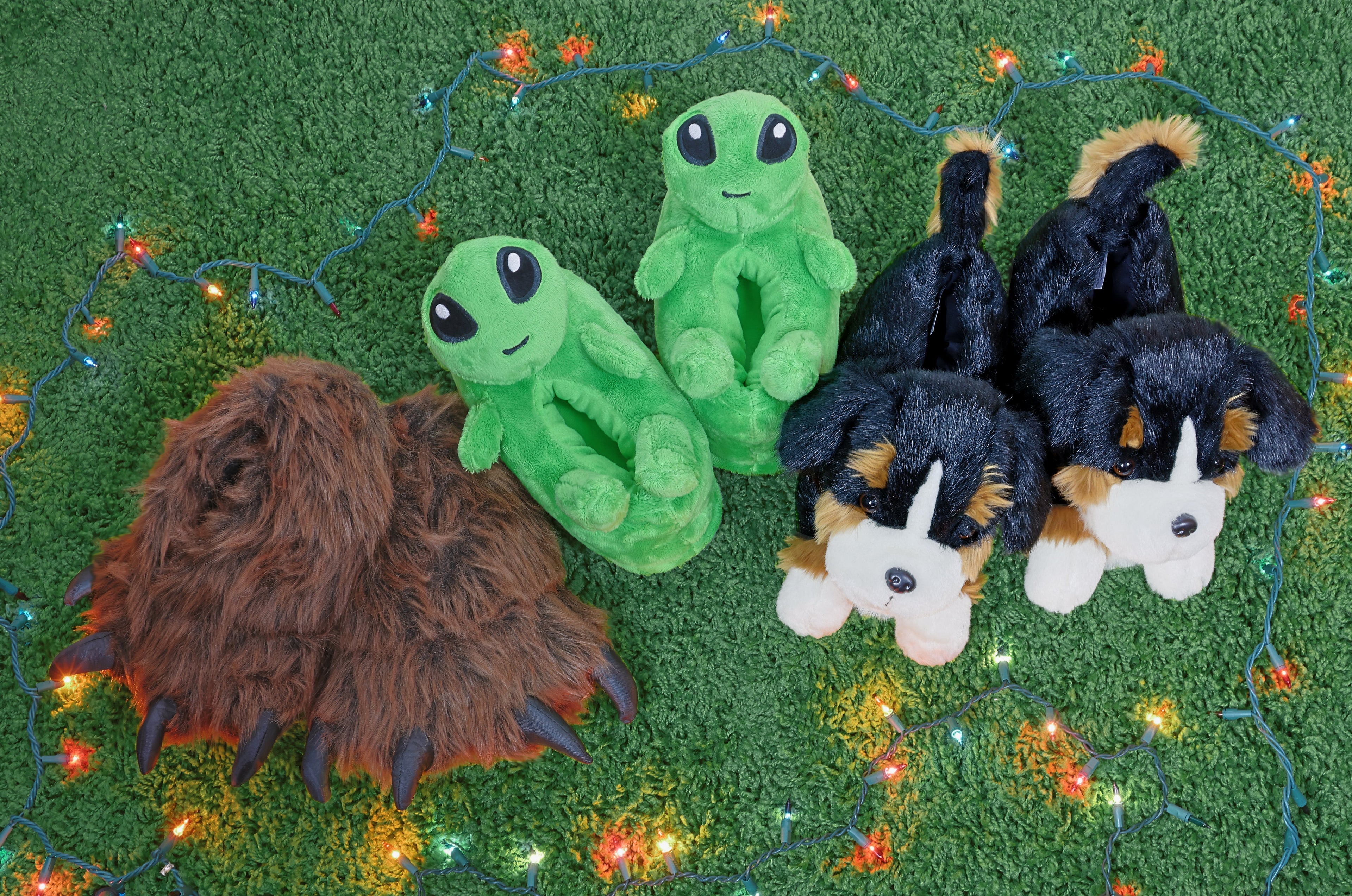 Three pair of slippers on a green carpet, surrounded by holiday lights