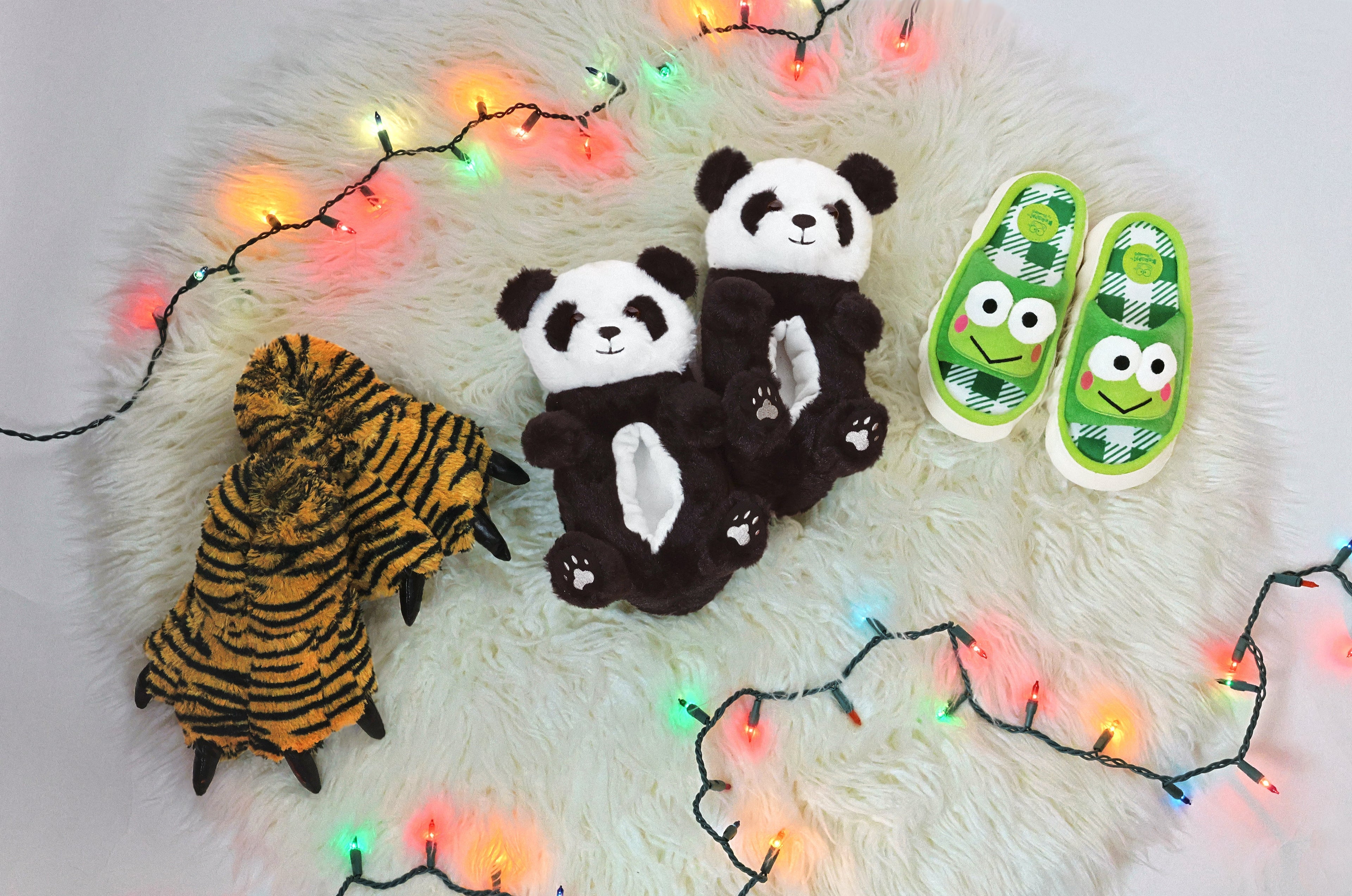Three pair of kids slippers on a white carpet with holiday lights around them
