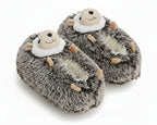 A pair of plush hedgehog slippers with gray and white faux fur, tan paws, and a face on the top, shown on a white background.
