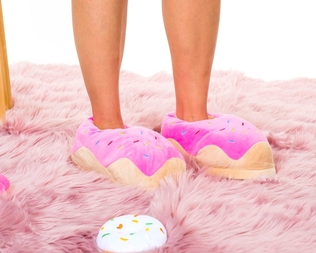 A person wearing oversized pink donut-shaped slippers with colorful sprinkles, standing on a fluffy pink rug.