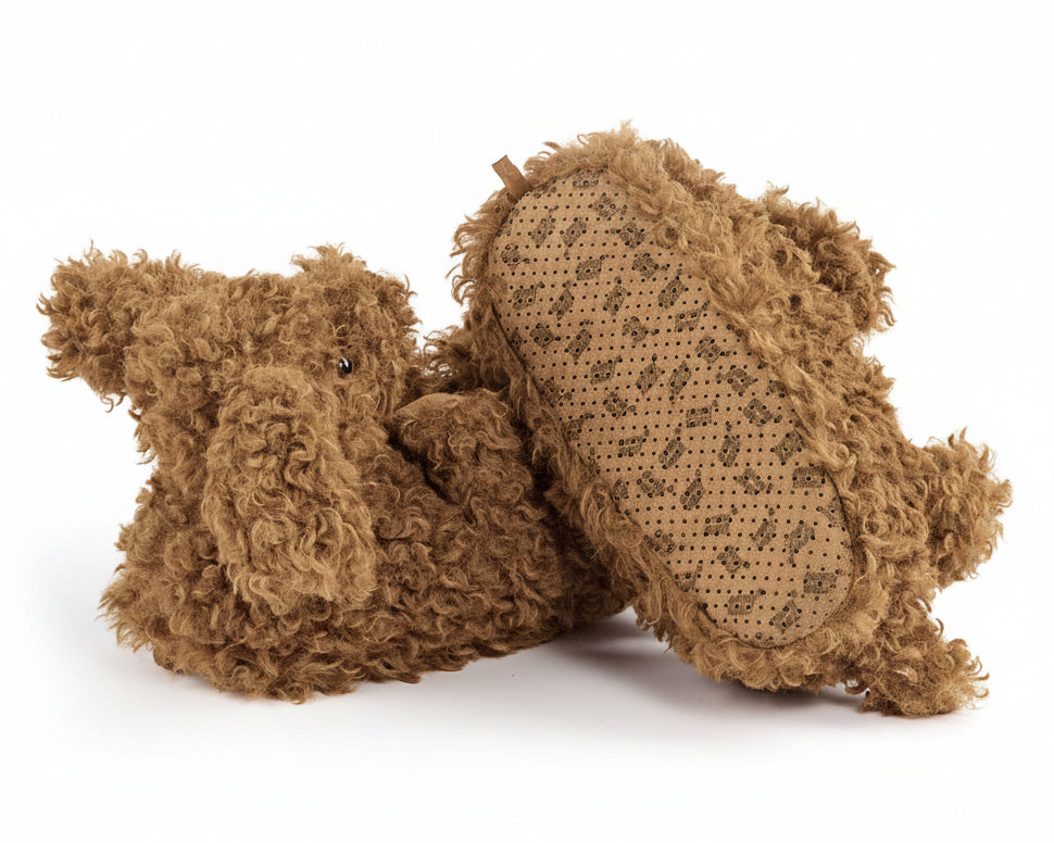 Pair of brown fuzzy doodle dog slippers on a white background.  One slipper is flipped to show the sole that has a repeating logo patter printed on the fabric and non-slip grips.
