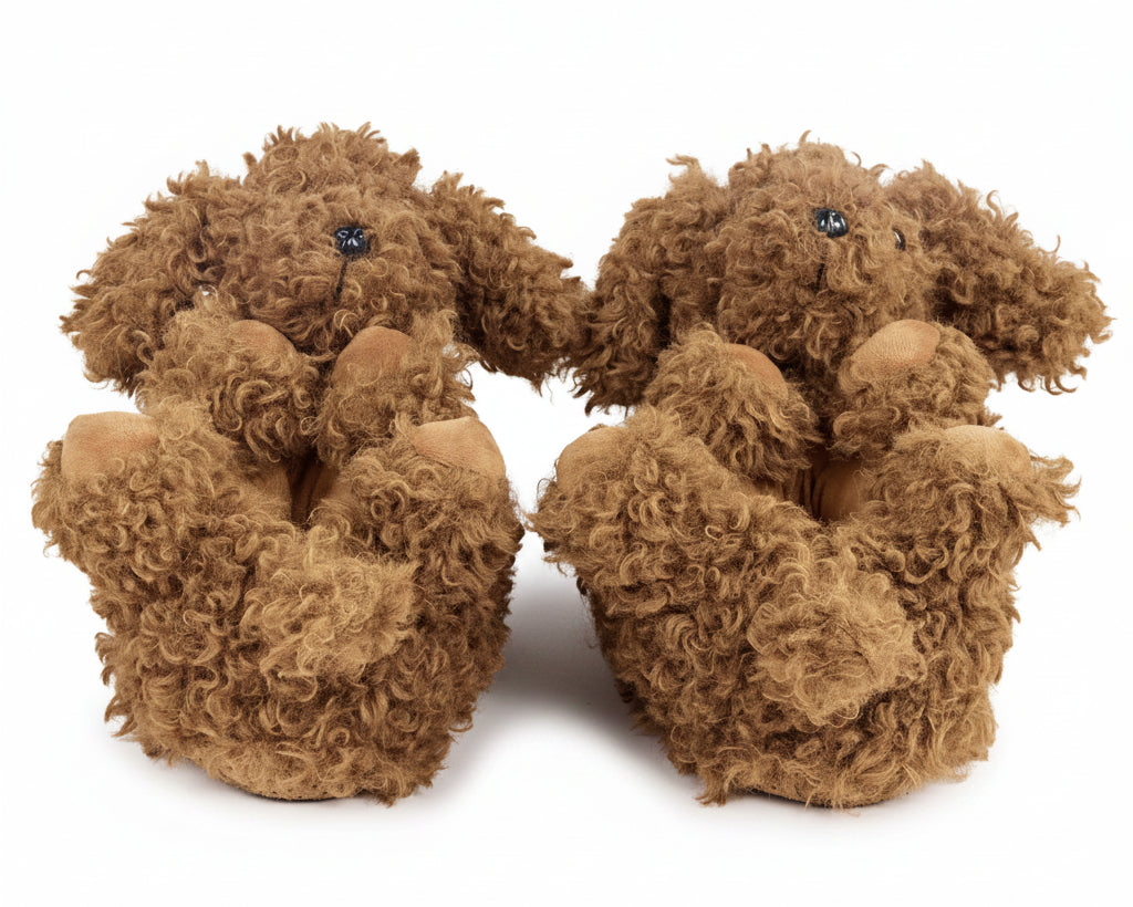 A pair of plush dog slippers in a curly brown faux fur material, featuring small black bead eyes and pinkish-tan paws and noses, set against a plain white background.