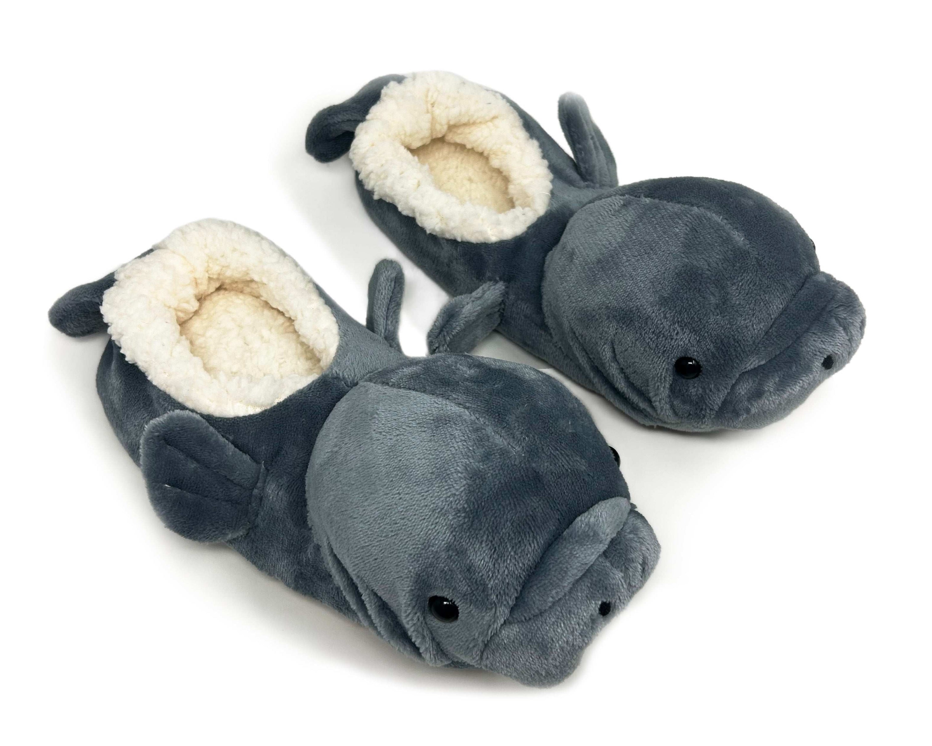A pair of plush manatee-shaped slippers in dark gray with a cream sherpa lining, shown on a plain white background.
