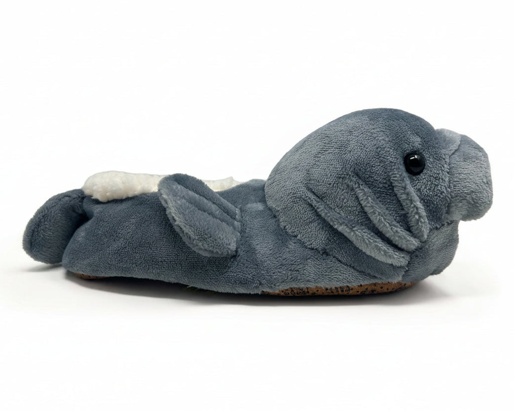 A plush manatee-shaped slipper in slate blue-gray fabric with a small white accent on the tail and a black bead eye, photographed on a clean white background.