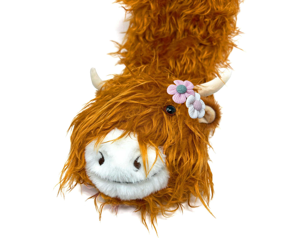 Plush head of a highland cattle with orange hair and a flower, on the front of a fuzzy sock, on a white background