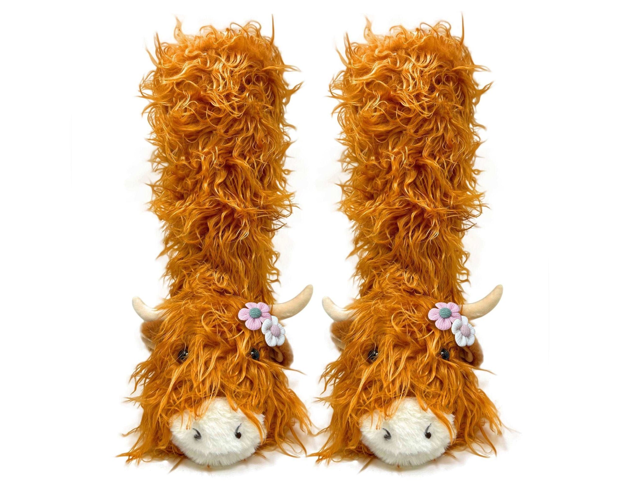 Two fluffy orange Highland cow slipper socks with white faces and horns on a white background