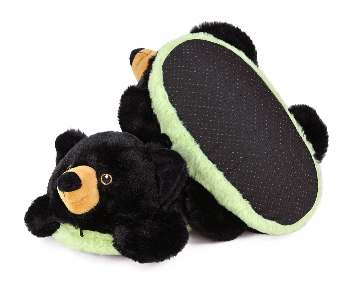 Pair of plush black bear slippers with green plush around the bottom.  One slipper is turned upside down to show non-slip grips on soles.