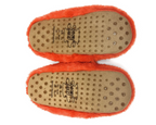 Bottom view of a pair of fluffy orange slippers showing the tan non-slip soles with printed brand markings and rubber grip dots.