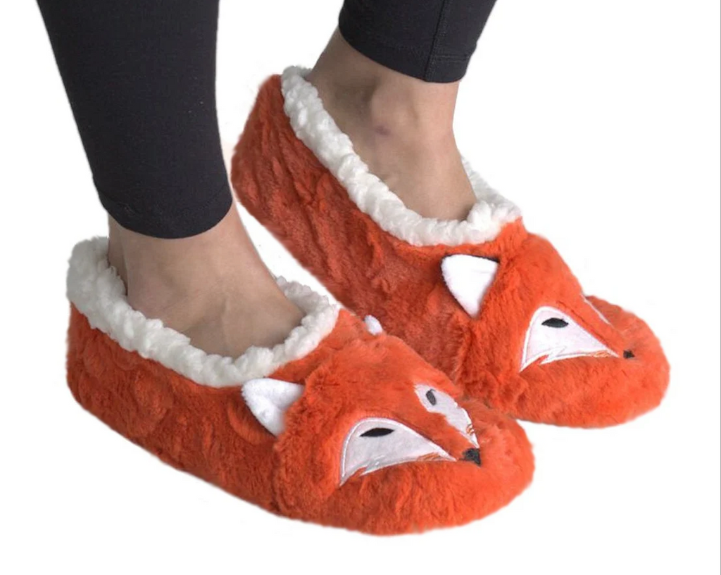 A pair of plush orange fox slippers with white faux-fur trim, shown being worn on a person's feet against a plain white background.